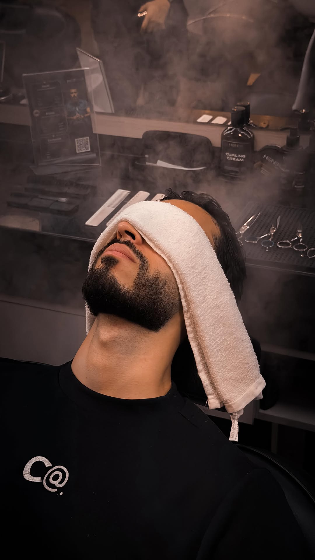 Cliente recebendo toalha quente no rosto durante serviço de barba